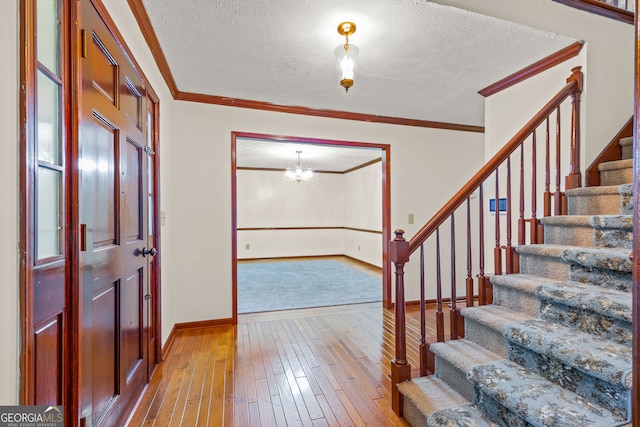 foyer featuring a textured ceiling, light wood-type flooring, stairs, and crown molding