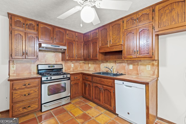 kitchen featuring stainless steel gas range oven, tile counters, under cabinet range hood, a sink, and dishwasher