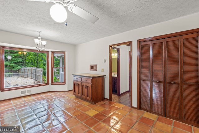 kitchen with a textured ceiling, brown cabinetry, ceiling fan with notable chandelier, visible vents, and decorative light fixtures