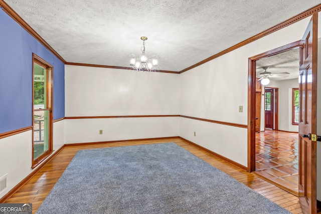 empty room featuring a textured ceiling, a notable chandelier, wood finished floors, baseboards, and ornamental molding