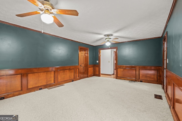 empty room featuring visible vents, light colored carpet, a textured ceiling, and wainscoting