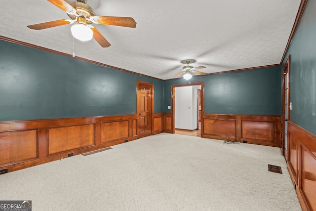 empty room with carpet flooring, a ceiling fan, and a wainscoted wall