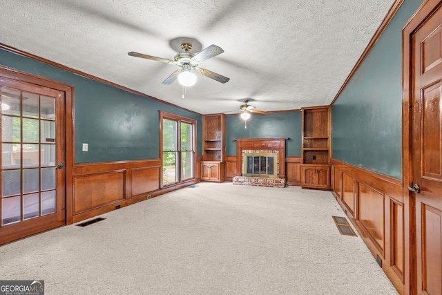 living room with a wainscoted wall, visible vents, light carpet, and a textured ceiling