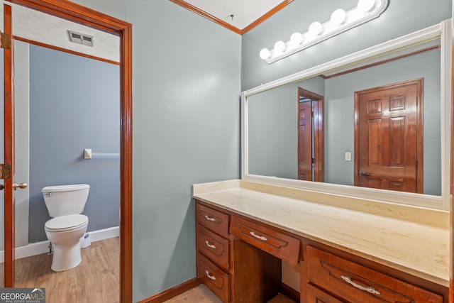 bathroom featuring toilet, wood finished floors, vanity, visible vents, and ornamental molding