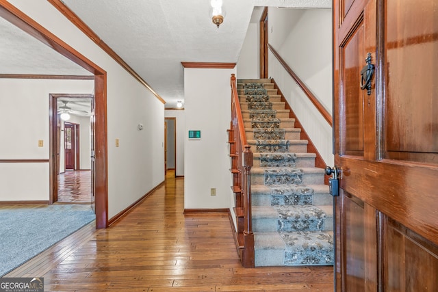 stairs with a textured ceiling, baseboards, wood finished floors, and crown molding