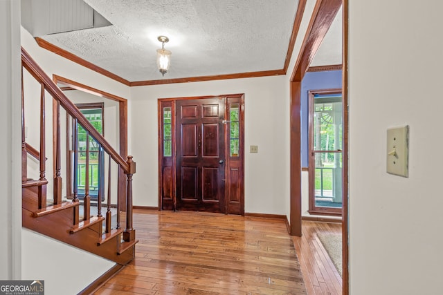 entryway featuring stairs, light wood-style flooring, ornamental molding, and a textured ceiling