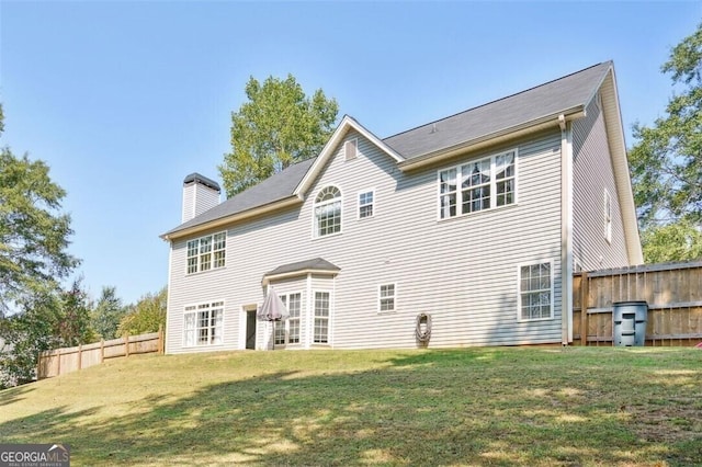 rear view of house with a yard, fence, and a chimney