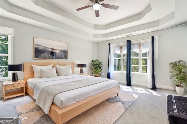 bedroom featuring ceiling fan, light colored carpet, visible vents, baseboards, and a raised ceiling