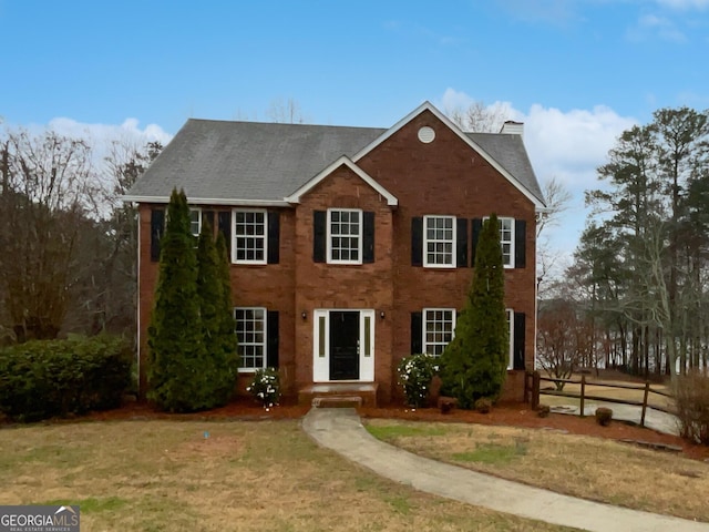 colonial-style house featuring a chimney, fence, and a front yard