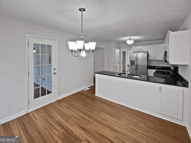 kitchen with stainless steel fridge, dark countertops, white cabinetry, pendant lighting, and a sink