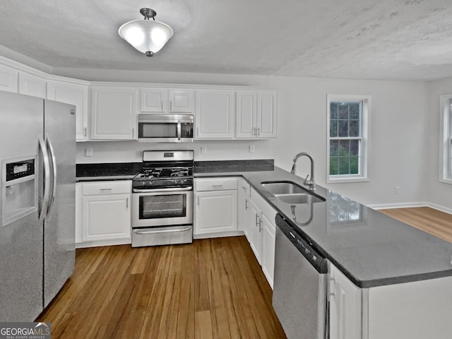 kitchen with stainless steel appliances, dark countertops, white cabinetry, and a sink