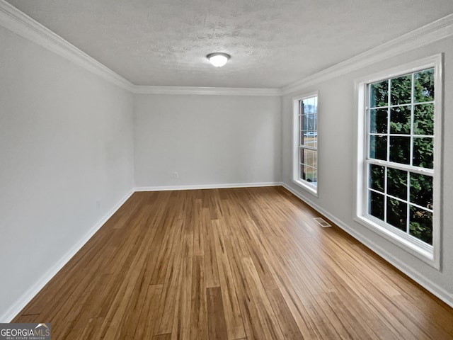 spare room with a textured ceiling, wood finished floors, visible vents, baseboards, and ornamental molding