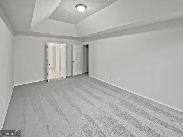 unfurnished bedroom with a textured ceiling, a tray ceiling, carpet flooring, and baseboards