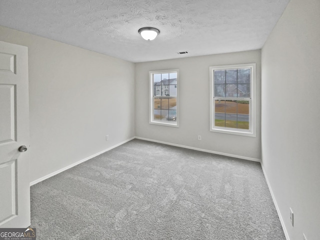 unfurnished room with carpet floors, baseboards, visible vents, and a textured ceiling