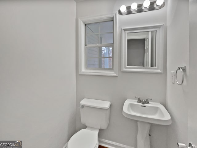 half bathroom featuring baseboards, a sink, and toilet