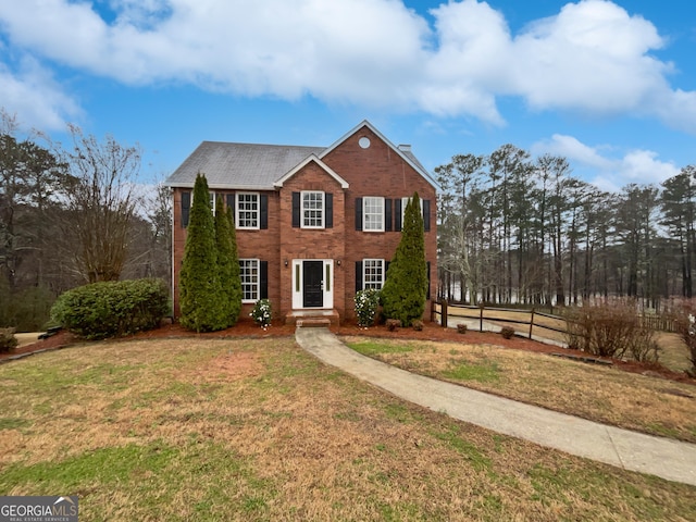 colonial home with brick siding, a front yard, and fence