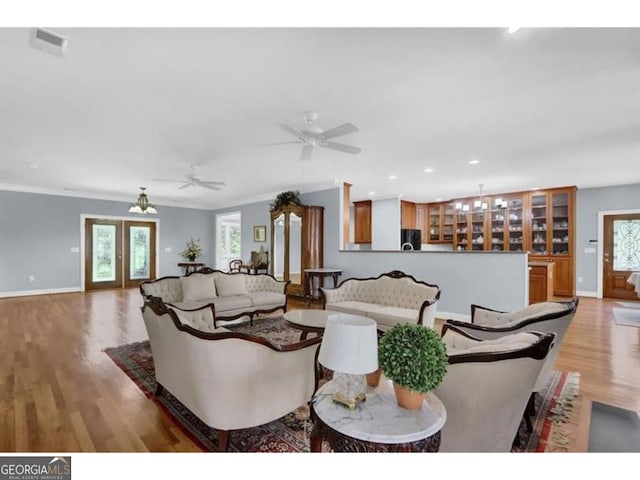 living area featuring baseboards, visible vents, ornamental molding, wood finished floors, and french doors