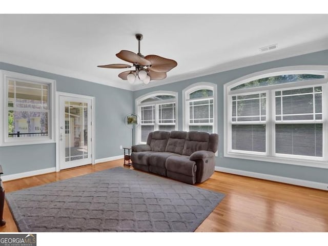 living room with wood finished floors, a ceiling fan, baseboards, visible vents, and crown molding