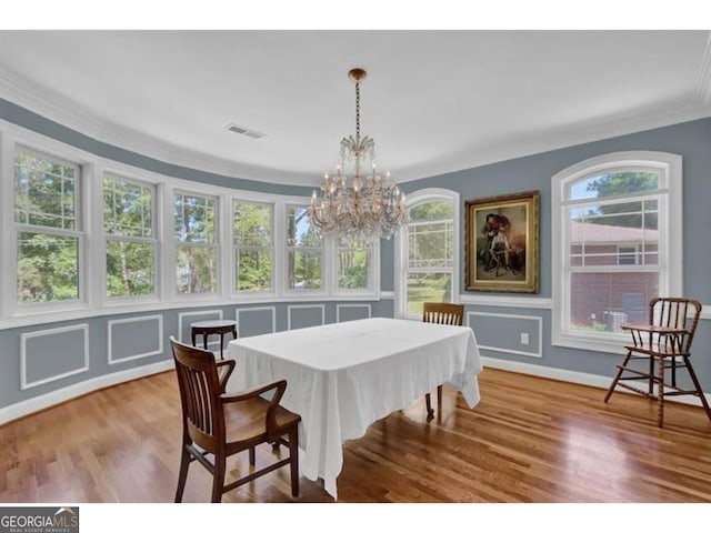 dining area featuring baseboards, visible vents, ornamental molding, wood finished floors, and a notable chandelier