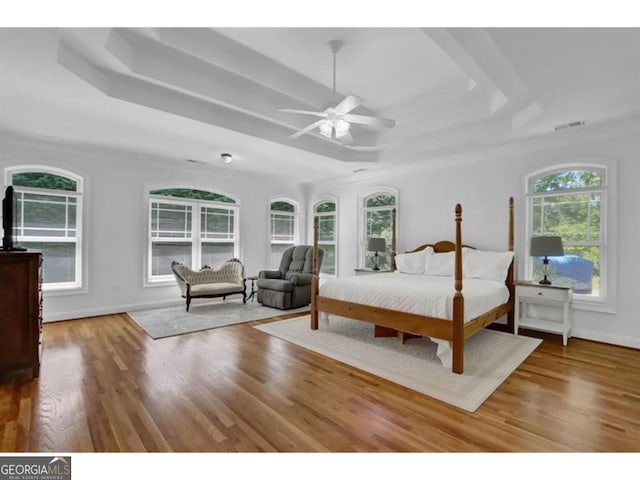 bedroom with baseboards, visible vents, ceiling fan, wood finished floors, and a tray ceiling