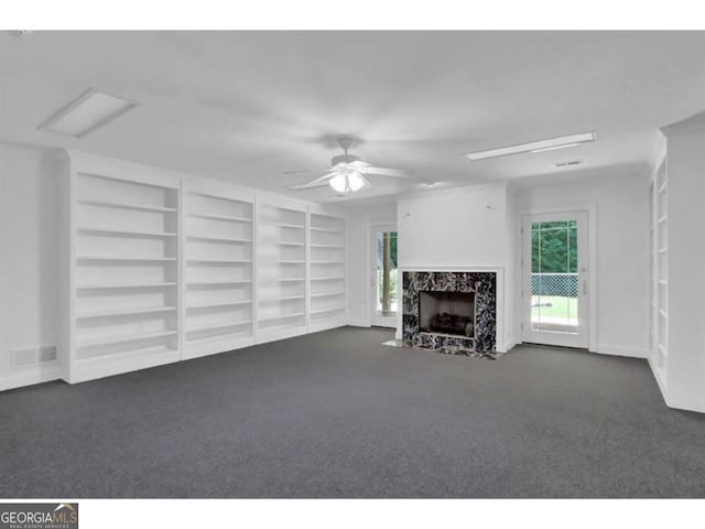 unfurnished living room featuring built in features, a high end fireplace, dark colored carpet, and a ceiling fan