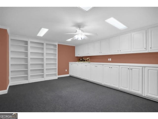 interior space with ceiling fan, baseboards, white cabinets, and dark colored carpet