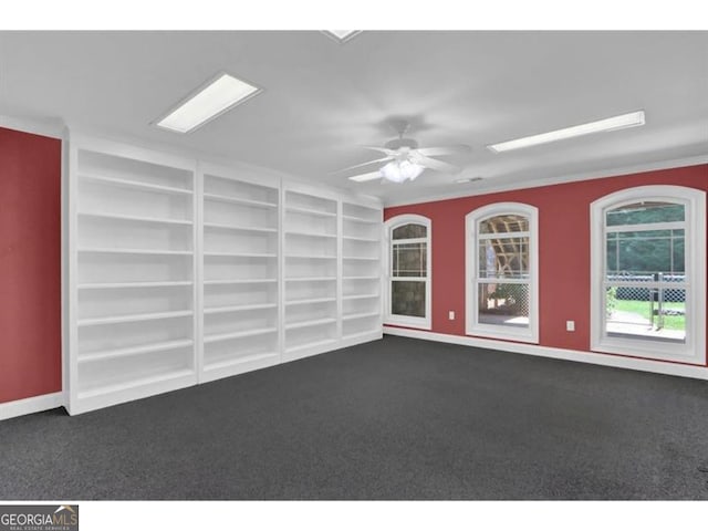 unfurnished room featuring ceiling fan, built in shelves, dark carpet, and baseboards