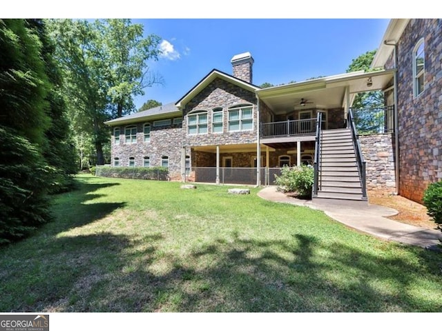 back of property featuring stone siding, a chimney, stairway, and a lawn