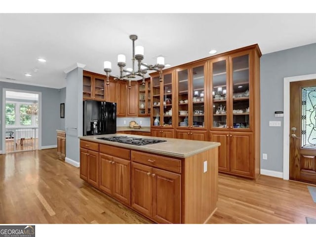 kitchen with light countertops, hanging light fixtures, brown cabinets, black refrigerator with ice dispenser, and glass insert cabinets