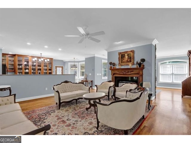 living room featuring a fireplace, ornamental molding, light wood-style floors, ceiling fan, and baseboards