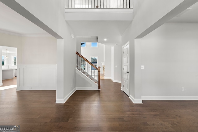 entryway with baseboards, a towering ceiling, ornamental molding, dark wood-style flooring, and stairs