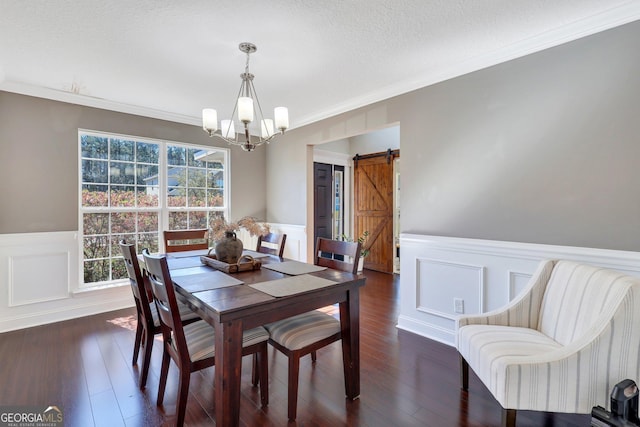 dining space featuring a barn door, dark wood-type flooring, ornamental molding, a textured ceiling, and a chandelier