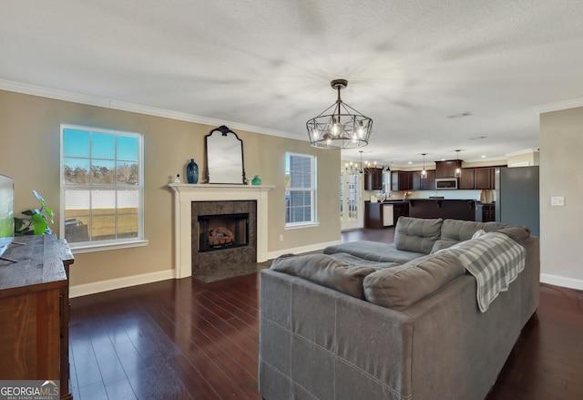 living room with baseboards, dark wood finished floors, a tiled fireplace, ornamental molding, and a chandelier