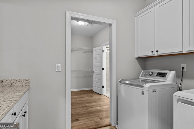 clothes washing area with washer and clothes dryer, visible vents, cabinet space, wood finished floors, and baseboards