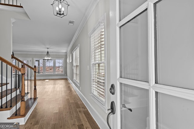 hallway with a notable chandelier, wood finished floors, baseboards, stairway, and crown molding