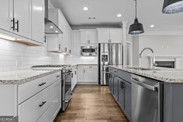 kitchen with white cabinets, wall chimney exhaust hood, stainless steel appliances, crown molding, and a sink