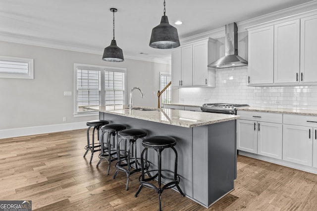 kitchen with ornamental molding, light wood-style floors, a sink, and wall chimney range hood