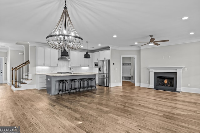 kitchen with wall chimney exhaust hood, a kitchen breakfast bar, stainless steel appliances, crown molding, and light countertops