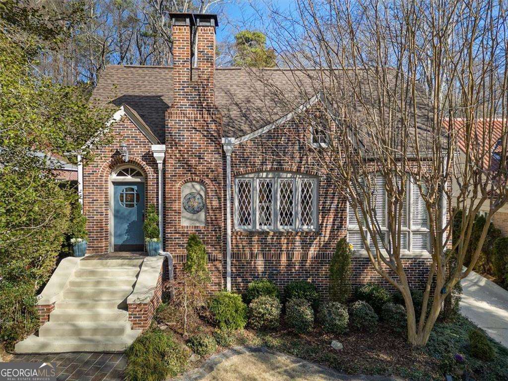 view of front of house with a shingled roof, brick siding, and a chimney