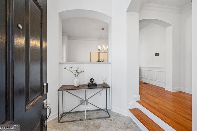 foyer entrance with arched walkways, ornamental molding, an inviting chandelier, light wood-style floors, and a decorative wall