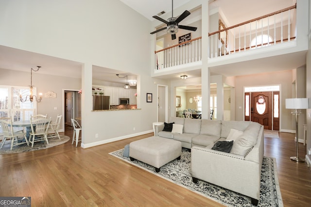 living area with ceiling fan with notable chandelier, wood finished floors, visible vents, and baseboards