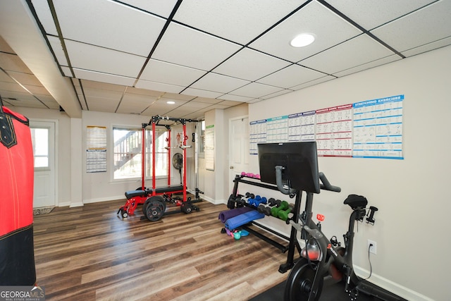 exercise room with a paneled ceiling, baseboards, and wood finished floors