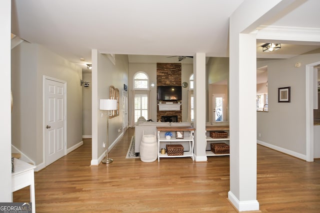 foyer with light wood-style floors, a stone fireplace, and baseboards