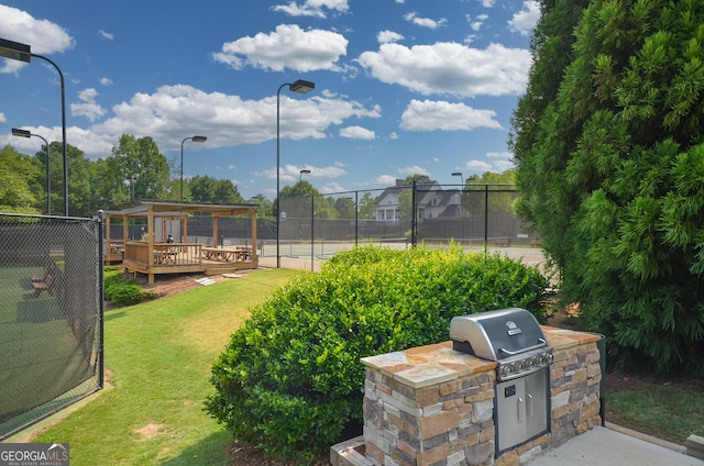 view of sport court with fence, an outdoor kitchen, a lawn, and a wooden deck