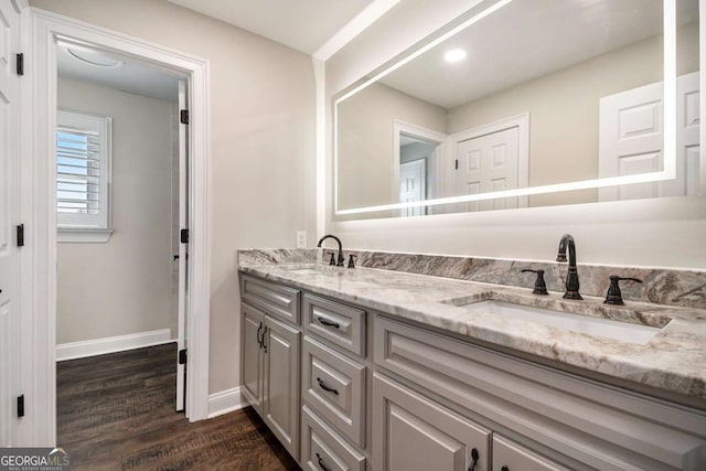 bathroom featuring double vanity, wood finished floors, a sink, and baseboards