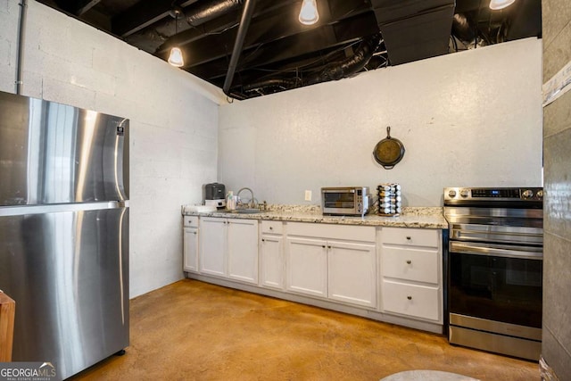 kitchen featuring a toaster, white cabinets, appliances with stainless steel finishes, light stone countertops, and concrete floors