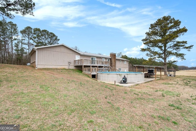 rear view of house with a deck, a lawn, and an outdoor pool