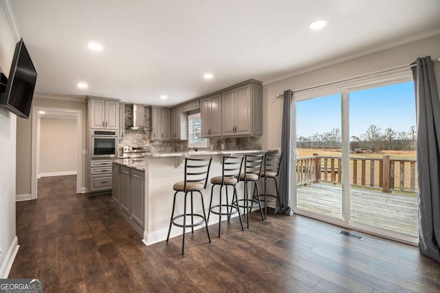 kitchen with gray cabinetry, a breakfast bar, visible vents, wall chimney range hood, and appliances with stainless steel finishes