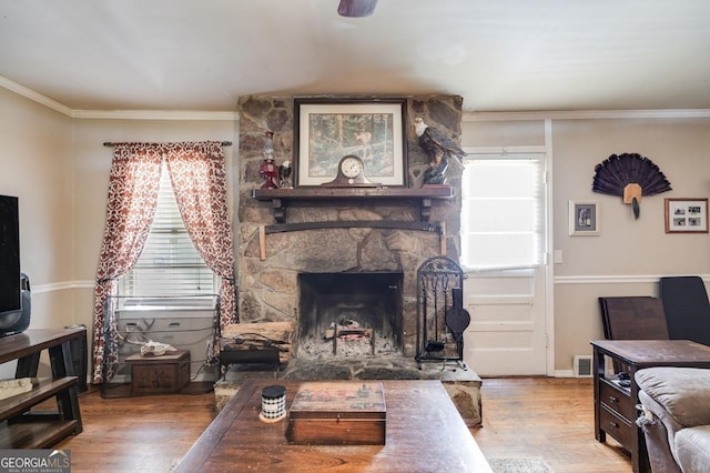 living area featuring ornamental molding, a healthy amount of sunlight, a fireplace, and wood finished floors