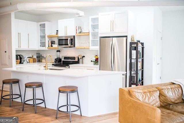 kitchen featuring light wood-style flooring, stainless steel appliances, a kitchen bar, open shelves, and a sink